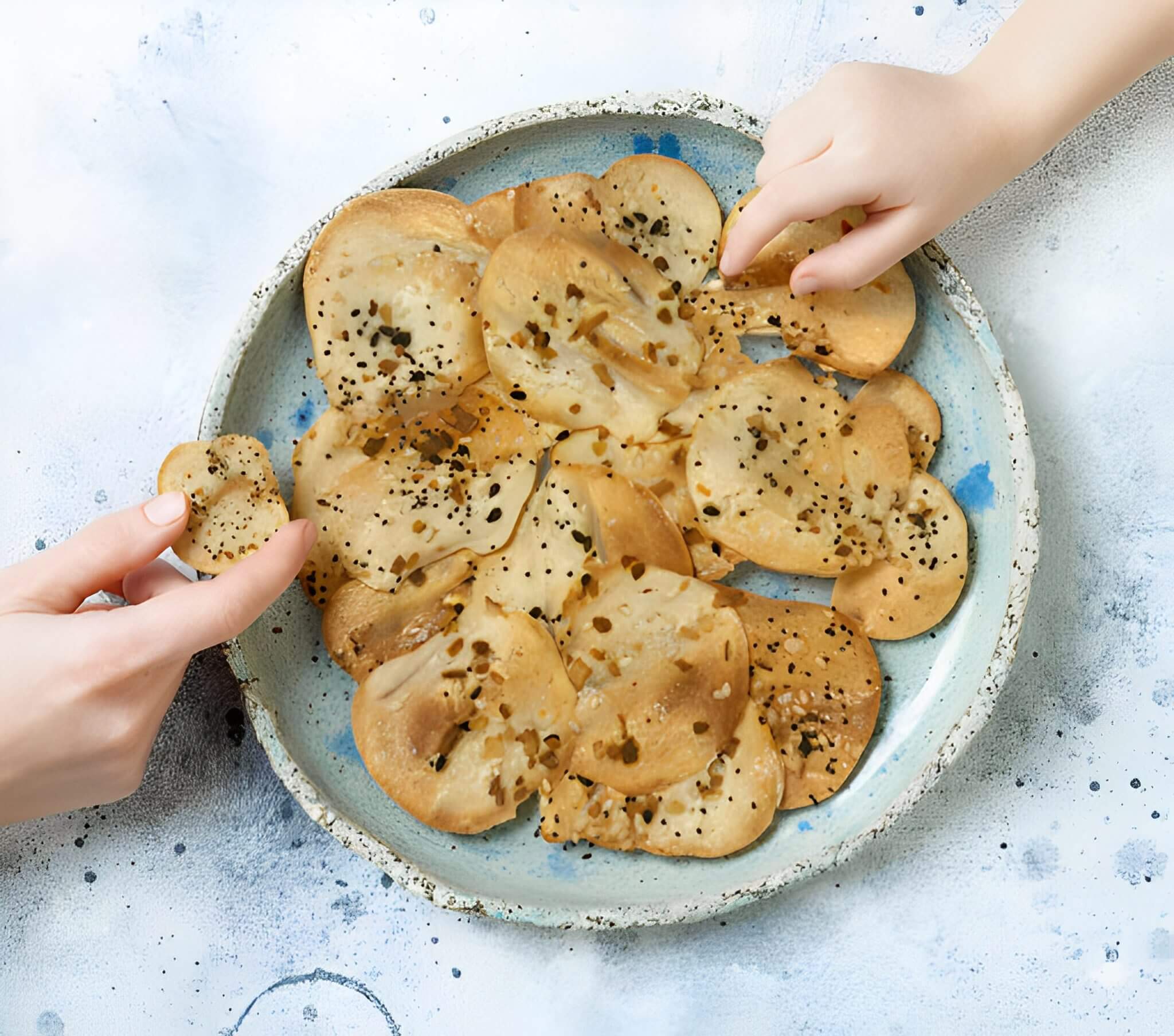 Two hands reaching for a plate of thinly sliced, seasoned chips.